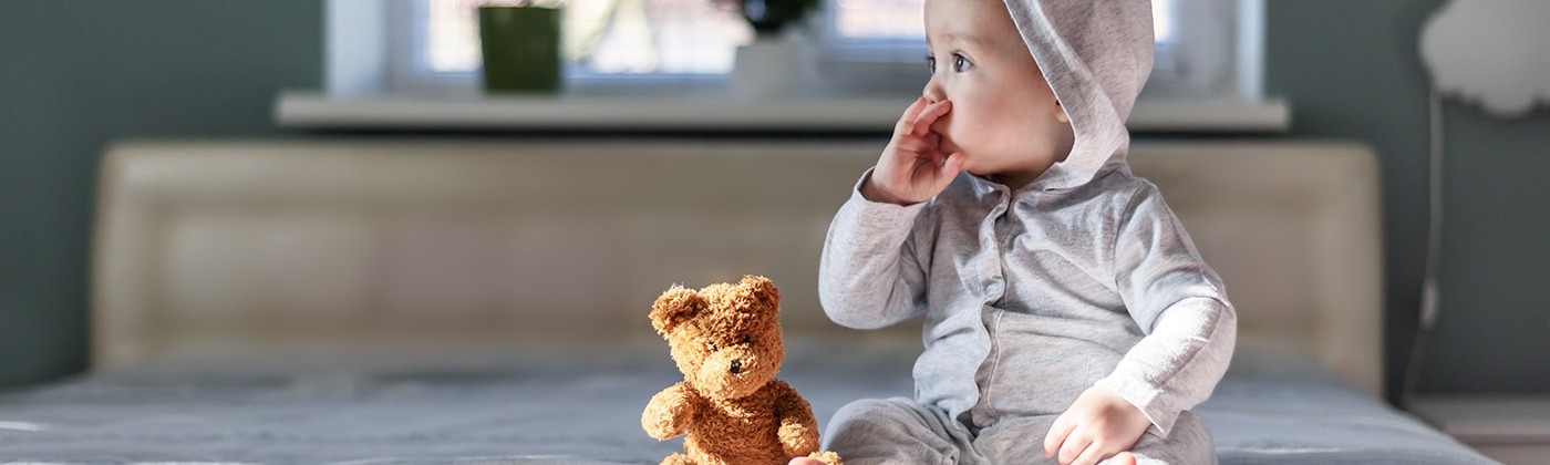 Baby sitting on bed with teddy bear