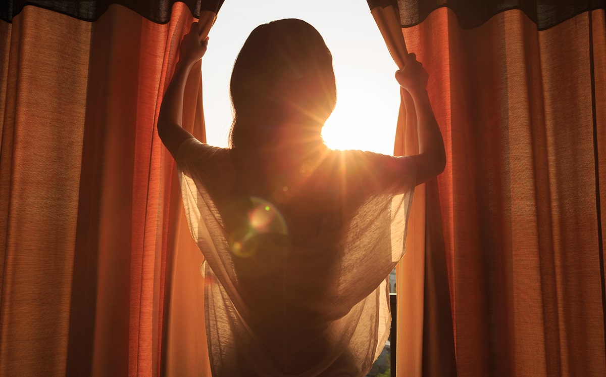 Woman opening curtains to bright sun