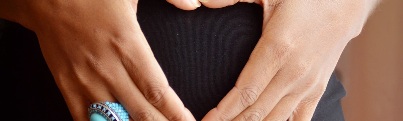 Pregnant woman with hands in heart shape over stomach