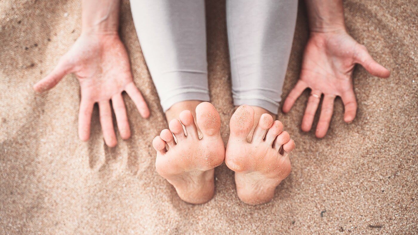 woman's feet and hands sitting on sand